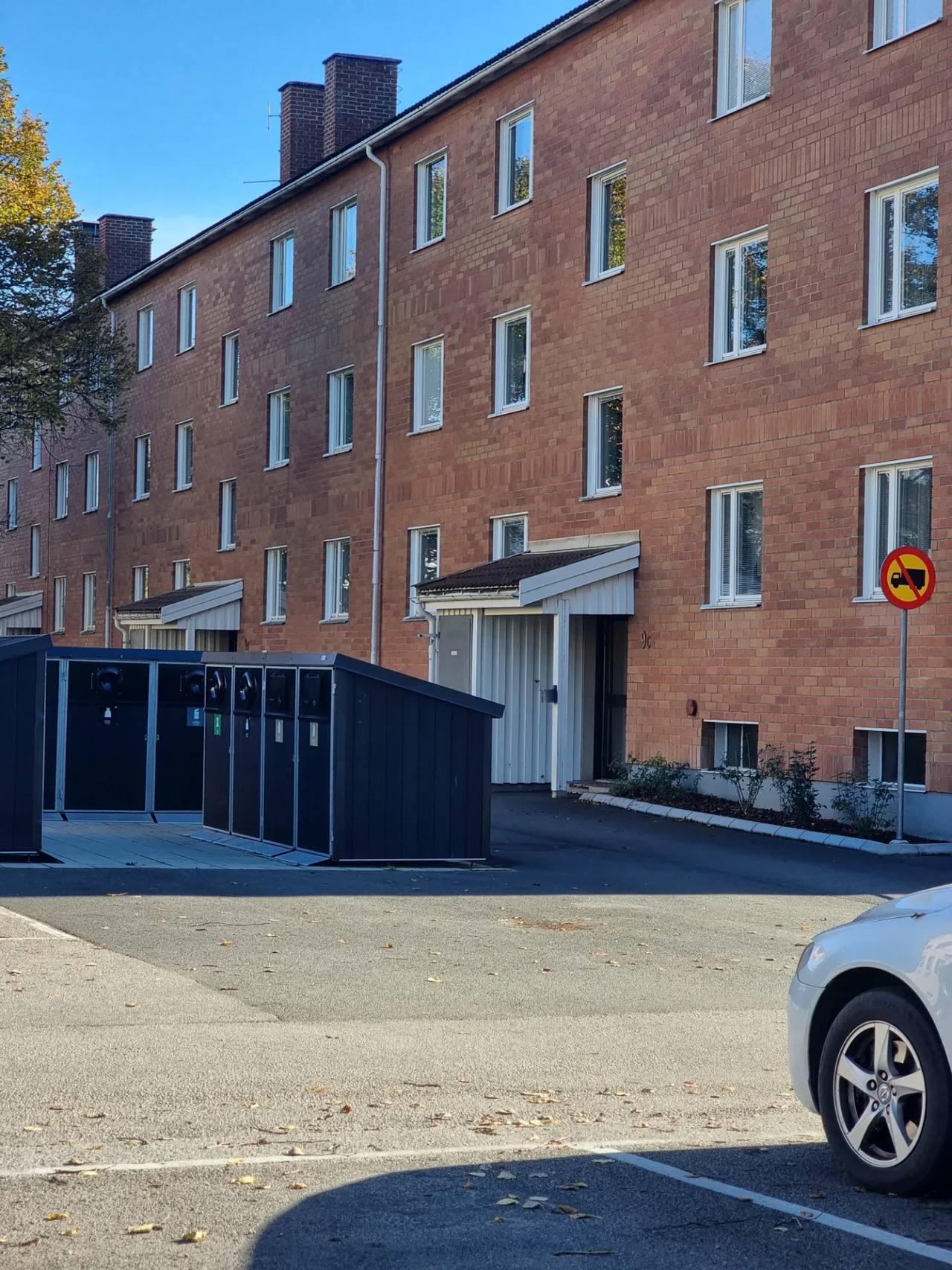 Tegeltrapphus med fönster och entréer, Töreboda. Soptunnor och parkering framför.